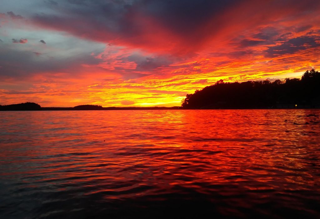 A vibrant, colorful sunset over a lake with a silhouette of a forest.