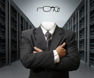 A headless businessman in a suit with his arms crossed, standing in a server room.
