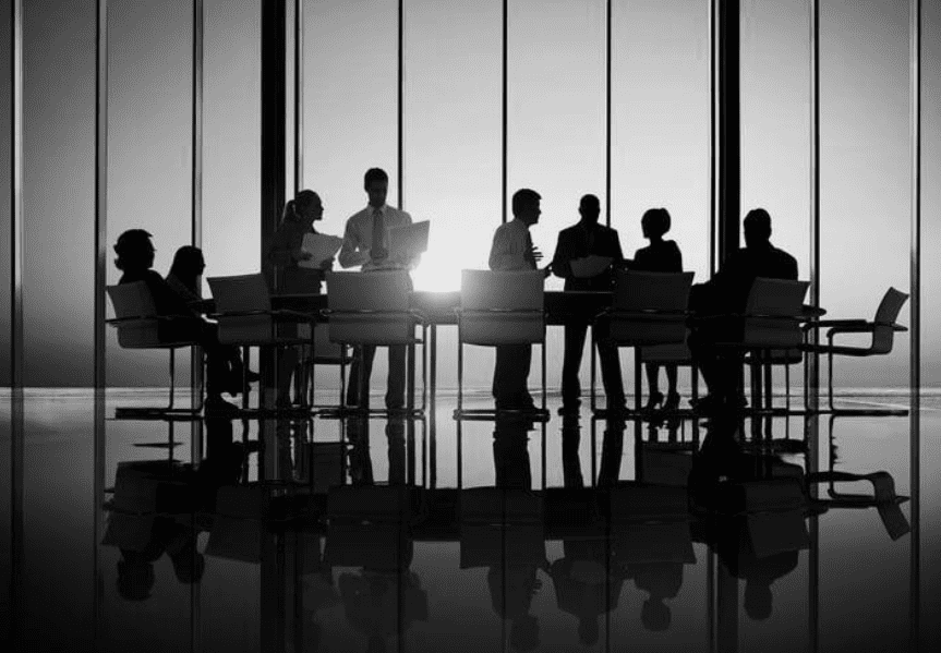 A black and white, silhouetted photo of business people in a meeting room with a large window.