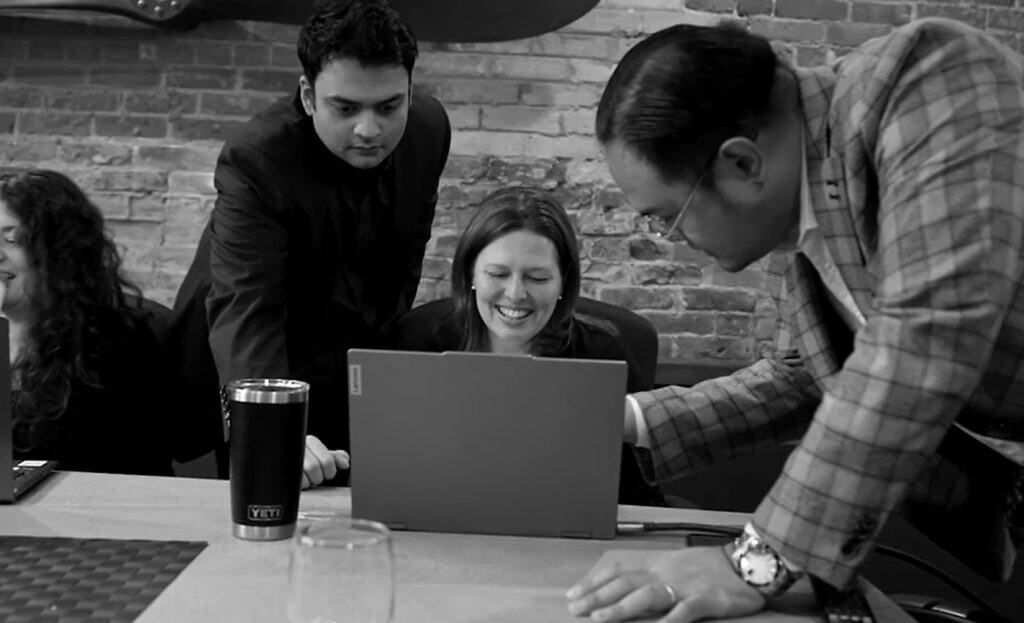 Team collaborating and smiling while reviewing work on a laptop in office